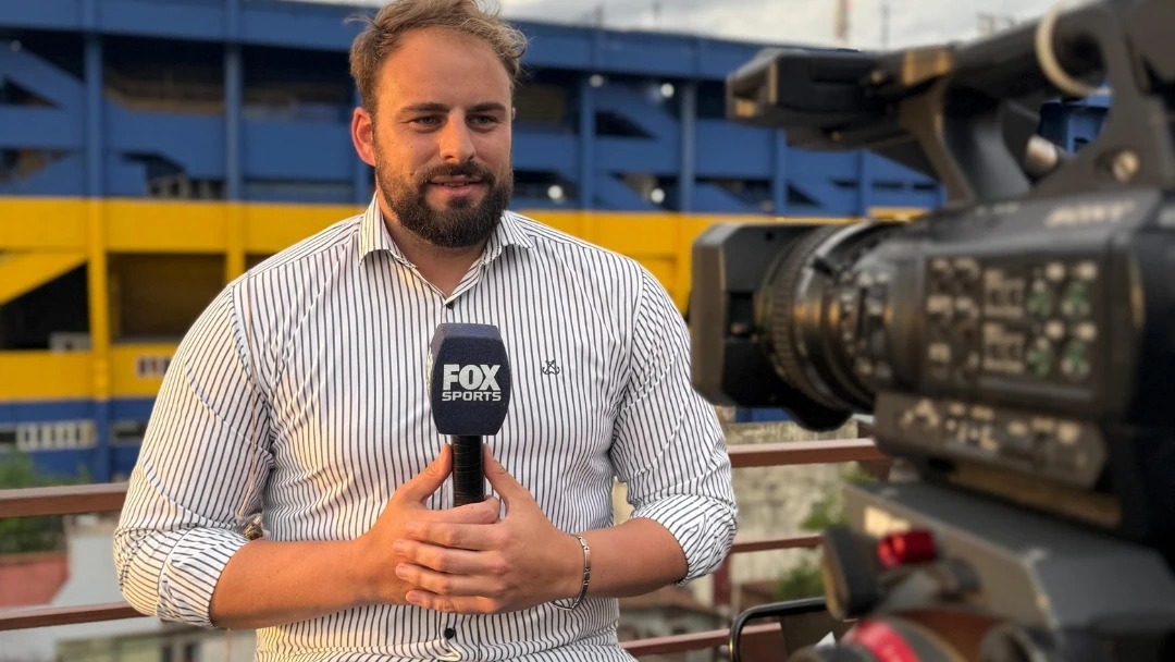 Ezequiel Polanco, cronista oficial de Boca Juniors, sostiene un micrófono de Fox Sports frente a La Bombonera